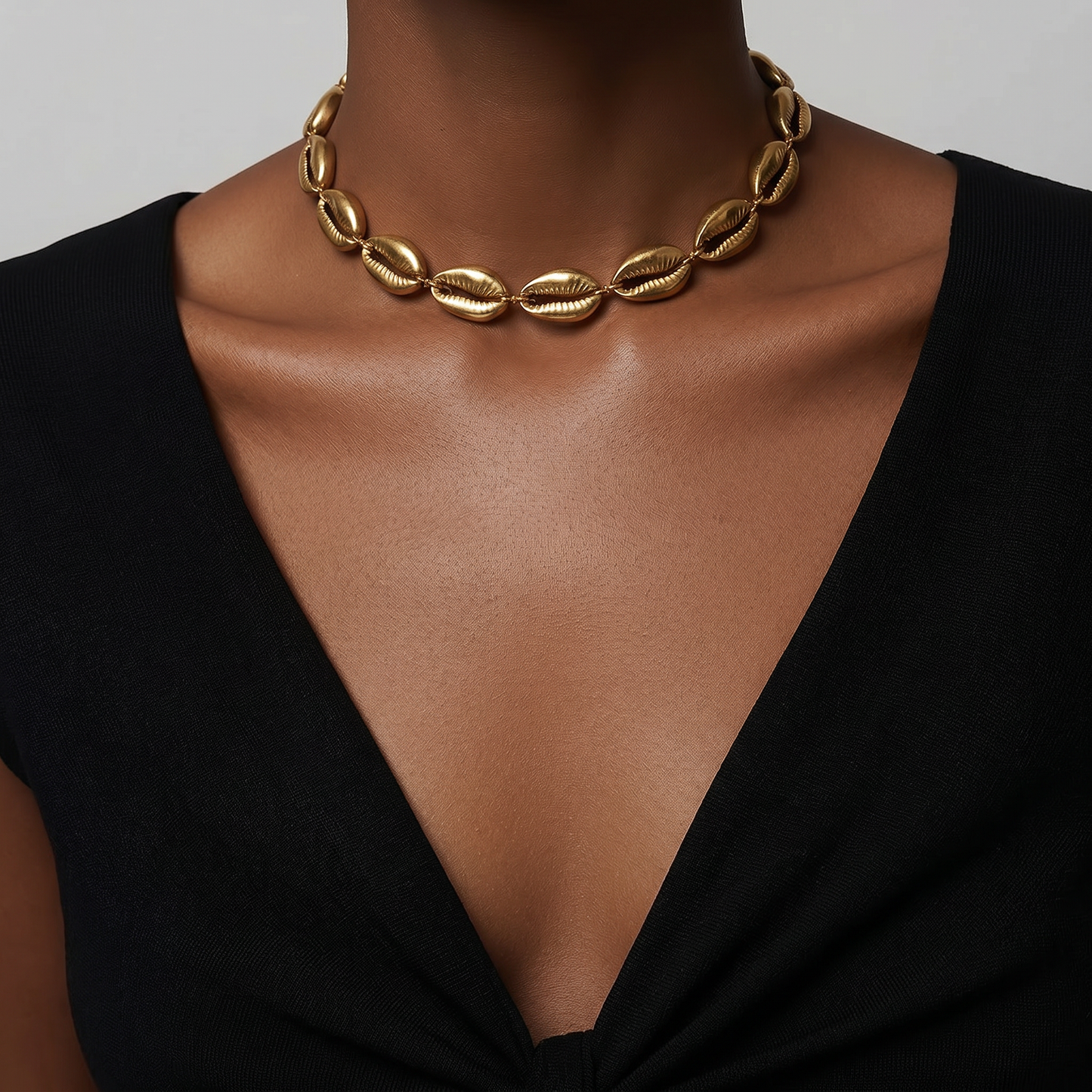 A close-up of a model wearing a chunky brass chain necklace made of elongated, textured shell-like.