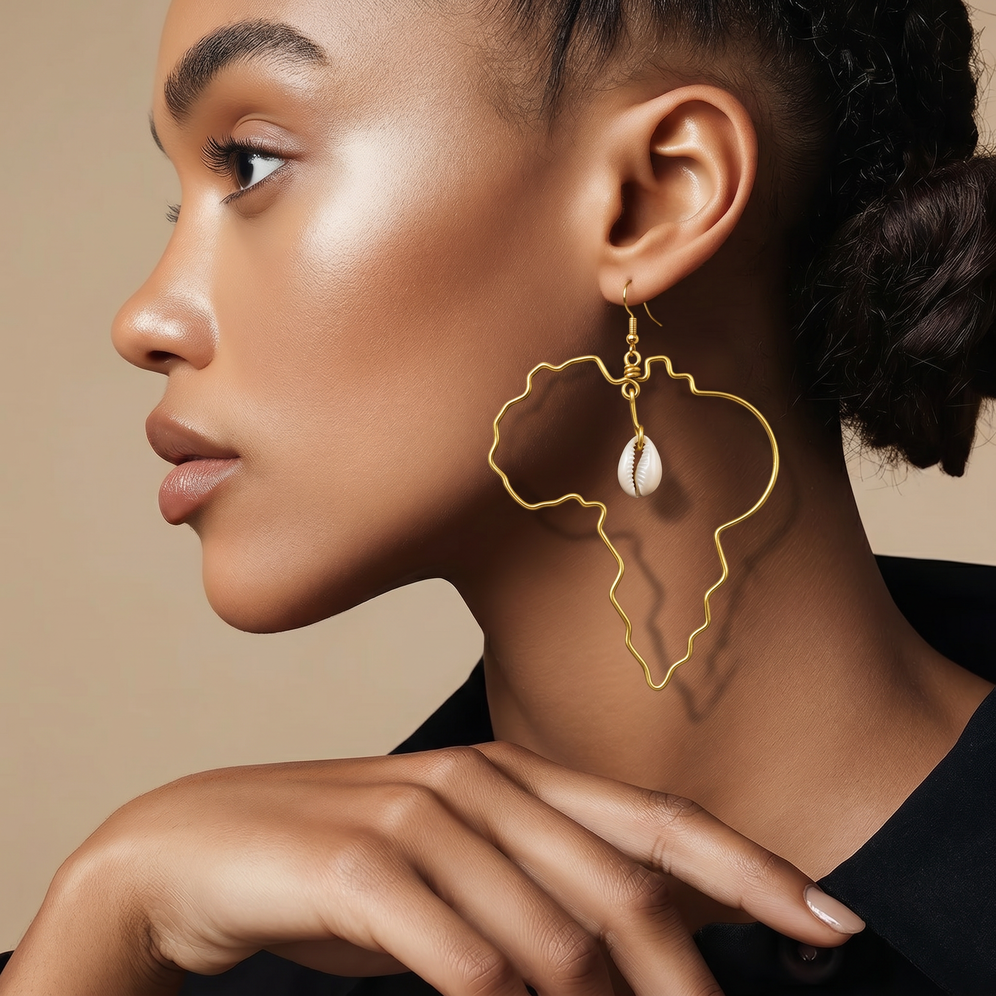 A close-up side profile of a woman wearing a large gold earring shaped like the outline of Africa, with a small white teardrop charm hanging from it.