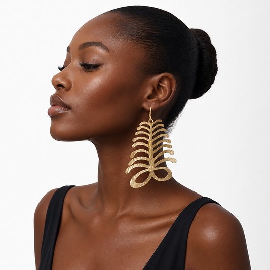 A woman in profile wearing a large, textured gold leaf-shaped dangle earring against a clean white background.