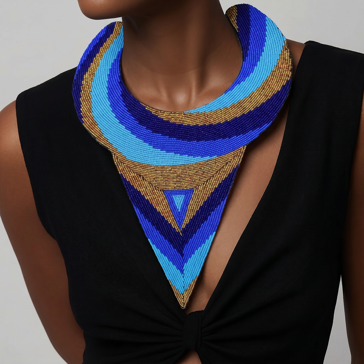 A close-up of a model wearing a large, geometric bib-style necklace made of blue, light blue, and gold beaded stripes, paired with a black sleeveless top.